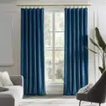 Salon lumineux décoré avec une paire de longs rideaux en velours bleu canard habillant une grande fenêtre blanche.