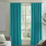 Rideaux couleur sarcelle ou turquoise, plissés, suspendus à une tringle dorée dans un salon moderne avec des murs clairs, un canapé gris et une plante.