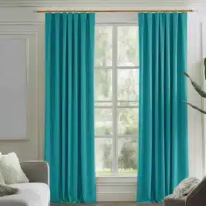 Rideaux couleur sarcelle ou turquoise, plissés, suspendus à une tringle dorée dans un salon moderne avec des murs clairs, un canapé gris et une plante.