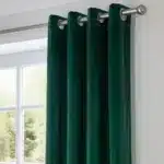 Vue rapprochée de la tête du rideau montrant la texture riche et soyeuse du velours vert émeraude ainsi que la finition à œillets métalliques sur la tringle.