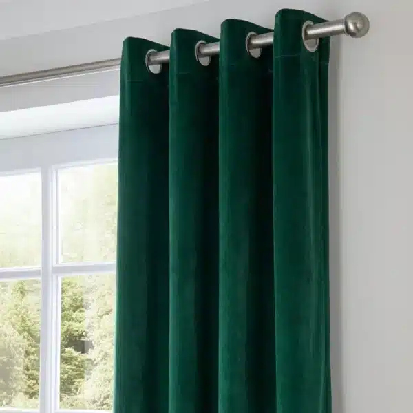 Vue rapprochée de la tête du rideau montrant la texture riche et soyeuse du velours vert émeraude ainsi que la finition à œillets métalliques sur la tringle.