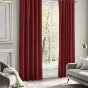 Gros plan sur des rideaux rouge foncé recouvrant une fenêtre, avec une chaise grise et un canapé gris visibles en arrière-plan dans un salon.
