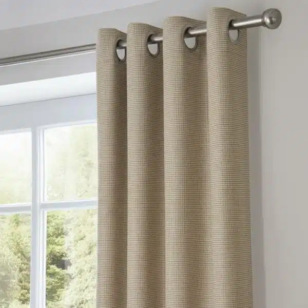 Rideau beige suspendu à une tringle métallique à œillets. Le tissu a une texture de lin légèrement striée. La scène montre une fenêtre et une partie du mur intérieur.