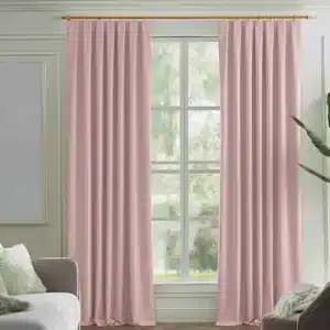 Rideaux couleur rose poudré, plissés, suspendus à une tringle dorée dans un salon moderne avec des murs clairs, un canapé gris et une plante verte.