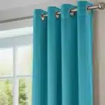 Gros plan sur des rideaux en tissu de couleur sarcelle ou turquoise, montrant le tissu, les plis et les œillets métalliques argentés sur une tringle.