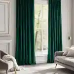 Coin lecture moderne avec fauteuil et lampadaire doré, mis en valeur par des rideaux en velours vert au tombé lourd et luxueux devant une grande fenêtre.