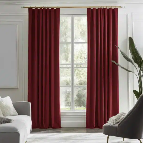 Rideaux bordeaux/rouge foncé, plissés, suspendus à une tringle dorée dans un salon moderne avec des murs blancs, un canapé gris, un fauteuil gris et une vue sur la verdure.