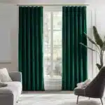Salon élégant et lumineux habillé de longs rideaux en velours vert émeraude profond, contrastant avec un canapé gris clair et des murs blancs moulurés.
