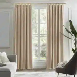Intérieur de salon moderne avec des rideaux en velours beige remplaçant les rideaux blancs, un canapé gris clair, un fauteuil gris foncé, et une grande plante verte, créant une atmosphère chic et naturelle.