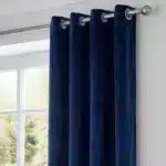Gros plan montrant la texture soyeuse du velours bleu nuit et la finition des œillets métalliques sur la tringle.