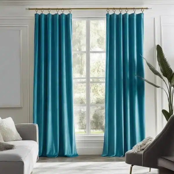 Grand salon lumineux décoré avec une paire de rideaux en velours ras couleur bleu paon sur une tringle dorée.