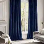 Fenêtre haute habillée de longs rideaux en velours couleur bleu nuit, apportant une touche cosy et chic à la pièce.