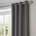 Rideau thermique épais gris anthracite installé sur une tringle en métal, vue rapprochée des œillets et du tombé.