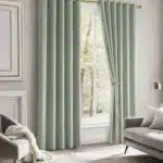 Rideaux thermiques épais verts décorant une pièce moderne et lumineuse avec fauteuil et lampe dorée.