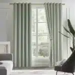 Rideaux thermiques épais verts installés dans un salon lumineux avec tringle dorée et grande fenêtre.