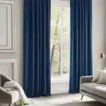 Rideaux en velours bleu roi à tête froncée ou plissée encadrant une grande fenêtre dans un salon moderne avec canapé gris.