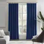 Paire de longs rideaux en velours bleu roi avec anneaux ou œillets visibles, suspendus dans un salon lumineux.